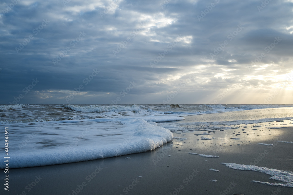 Sunset at the Beach with Sunbeams and Foam in the Water Sunset at the Beach with Sunbeams and Foam in the Water