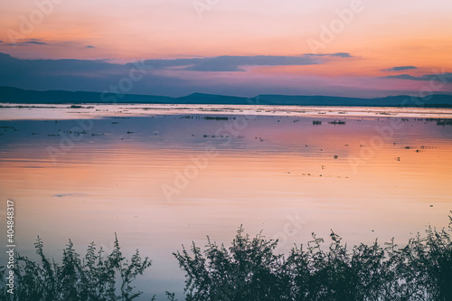 long exposure vanilla colorful sky and  lake reflection with mountains in the background. blurred wild grass blowing in the wind on foreground