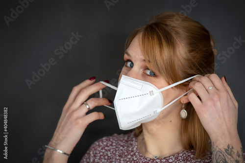 Junge blonde Frau zieht sich eine FFP2 Mundnasenschutz Maske auf - isoliert vor dunklem Hintergrund, viel Textfreiraum, Querformat