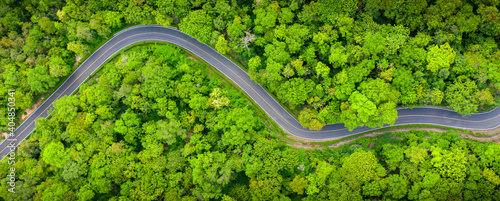 Winding road, top view of beautiful aerial view of asphalt road, highway through forest and fields in rainy season. For traveling and driving in nature. Banner panorama background.