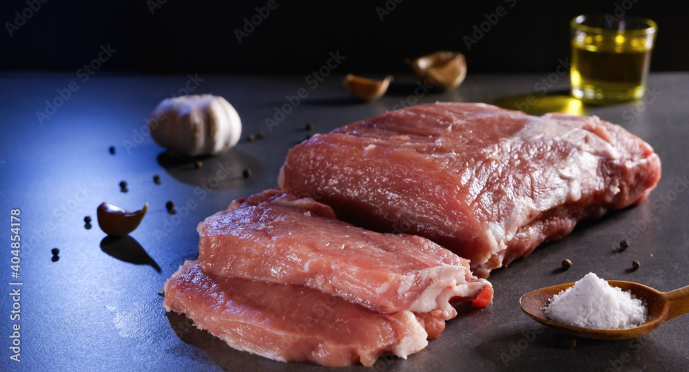 Raw meat. Juicy, appetizing chop with a piece and cut with spices and oil on a gray background.