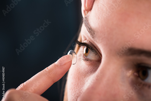 Detail of a contact lens on a woman's finger which is putting on lens to her eye on dark background. 