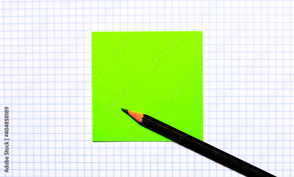 On a piece of checkered paper there is a green note sticker and a black pencil. Copy space