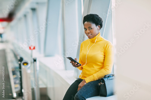 Attractive African girl is waiting for a train in the subway and listening to music with headphones