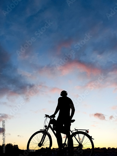 Fototapeta Naklejka Na Ścianę i Meble -  The silhouette of the guy against the blue sky, at sunset, the athlete on the evening walk, eco transport, health and beauty. Copy space.