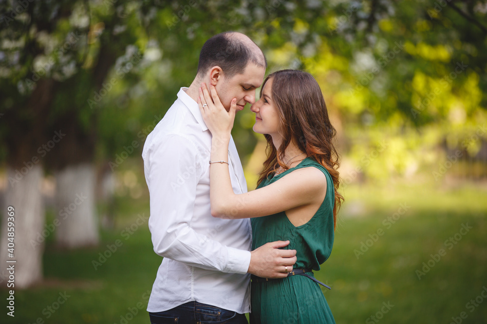 Fototapeta premium Young man and woman couple in a blooming apple garden. Tender holding each other. Spring lovestory. Brown-haired girl with long hairs. Young family