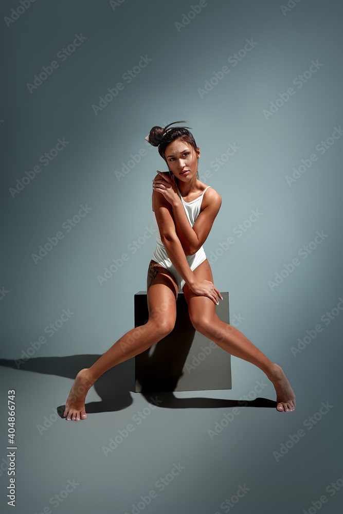 Sensual woman with long dark hair in white underwear sitting on gray cube over light grey studio background Sensual woman with long dark hair in white underwear sitting on gray cube over light grey studio background