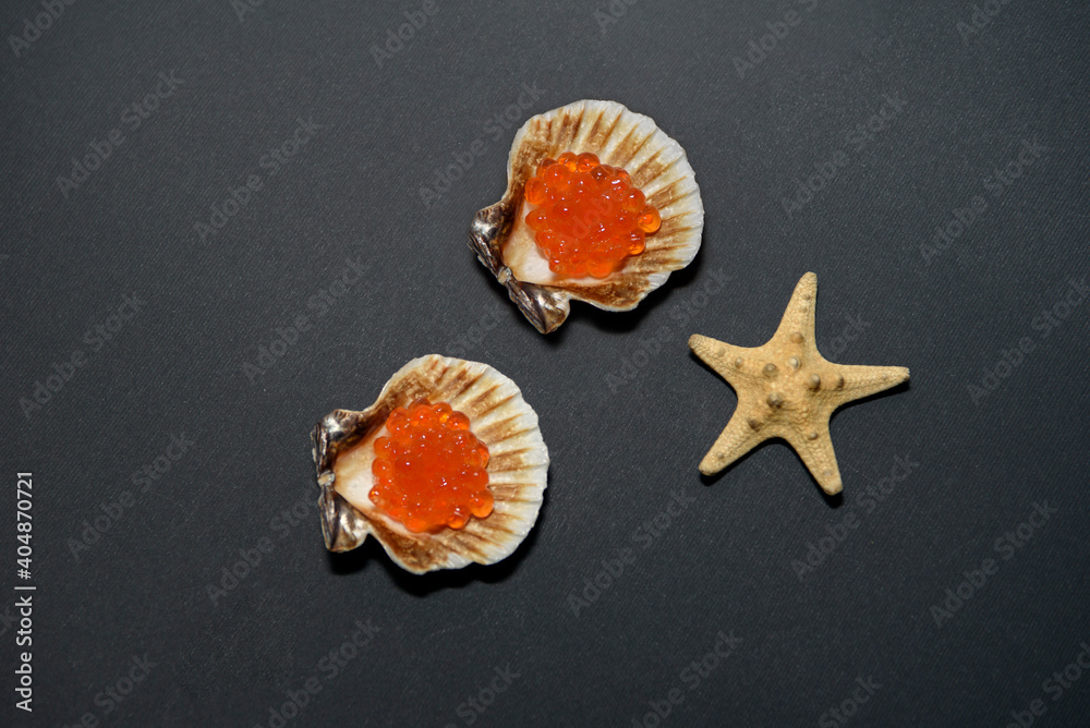 Red chum salmon caviar in an oyster shell, next to a starfish. Isolate on a black background. Red chum salmon caviar in an oyster shell, next to a starfish. Isolate on a black background.