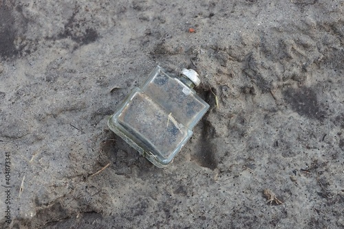 trash from one dirty white glass cologne bottle lies on gray ground outside