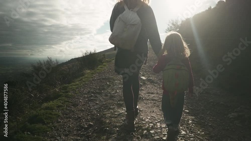 A little preschooler is walking hand in hand with his mother on a hillside in the autumn