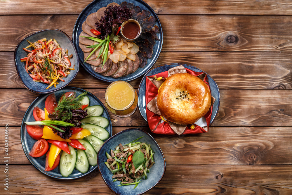 Flat layout of various dishes with sliced vegetables, meat cuts, salads, orange juice and bun on a brown wooden background. Flat layout of various dishes with sliced vegetables, meat cuts, salads, orange juice and bun on a brown wooden background.