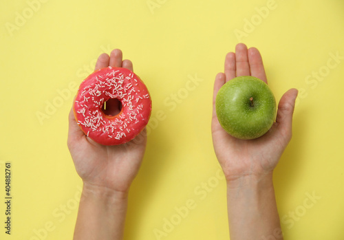 Top view of woman choosing between doughnut and healthy apple on yellow background, closeup