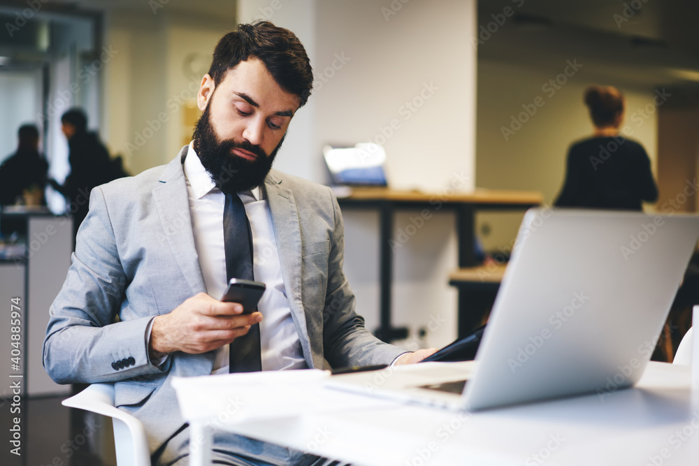 Businessman using smartphone while working on laptop in office