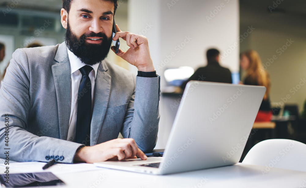 Bearded businessman using laptop and having phone call Bearded businessman using laptop and having phone call