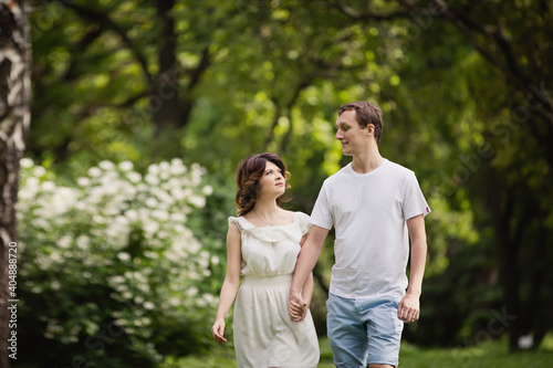Young man and woman couple in a blooming garden near jasmine bush. Tender holding each other. Spring love story. Brown-haired girl with long hairs with her boyfriend or husband. Young couple on a date