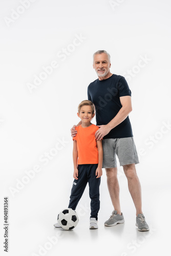 happy man hugging shoulders of grandson near soccer ball on white