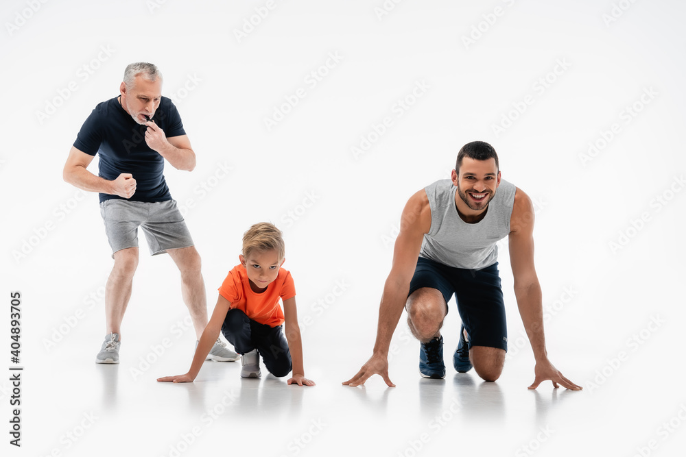 mature man whistling near father and son in low start position on white