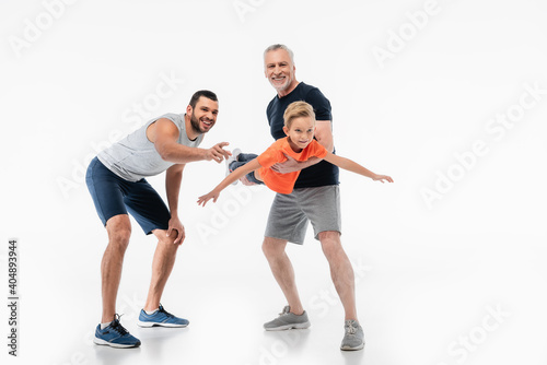 happy grandpa holding kid imitating flight near man pointing with finger on white