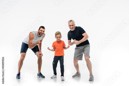 boy with dad and grandfather in sportswear demonstrating strength while smiling at camera on white