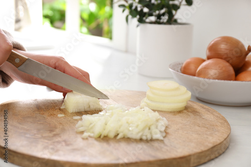 Woman chopping white onion on wooden board at table, closeup