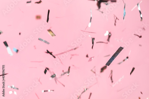 Shiny silver confetti falling down on pink background