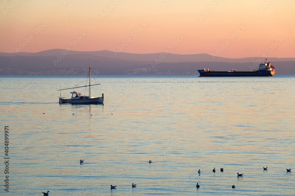 Flock of seagulls and boat during beautiful sunset. Landscape in Split, Croatia.