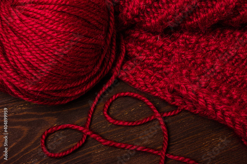 Knitting at your leisure. Red or burgundy color of woolen threads and a ball. Knitted fabric. Dark wood background