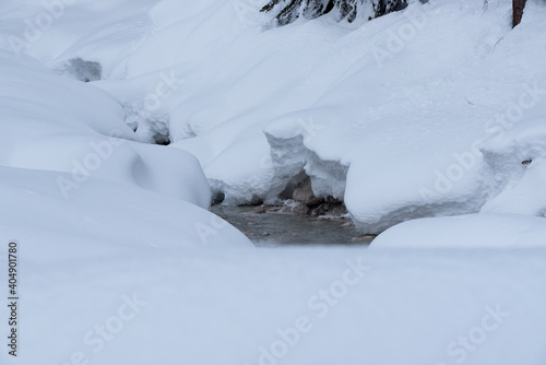 un torrente in montagna circondato da cumuli di neve arrotondati creano un ambiente morbido e luminoso  la neve si accumula sulle pietre ai lati di un torrente