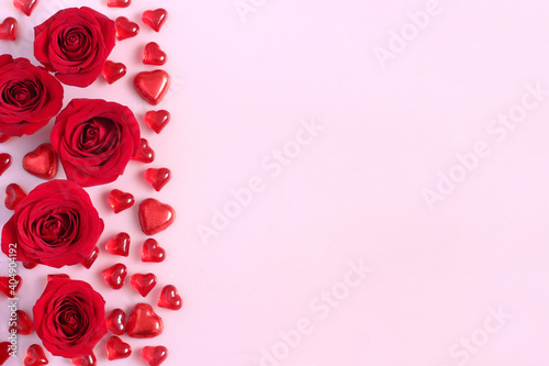 Red roses and heart shaped candies on pastel pink background. Space for text. 