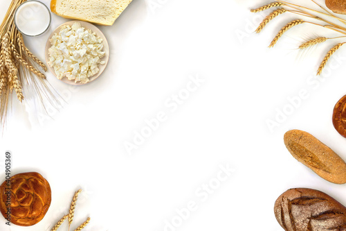 Frame of cheese, barley and wheat and milk in glass, different fresh baked bread, on a white background with space for text. Top view, flat lay