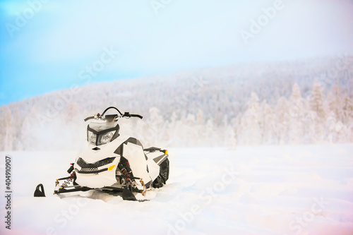 White snowmobile is standing on a snowy field on a background of a winter scenic landscape