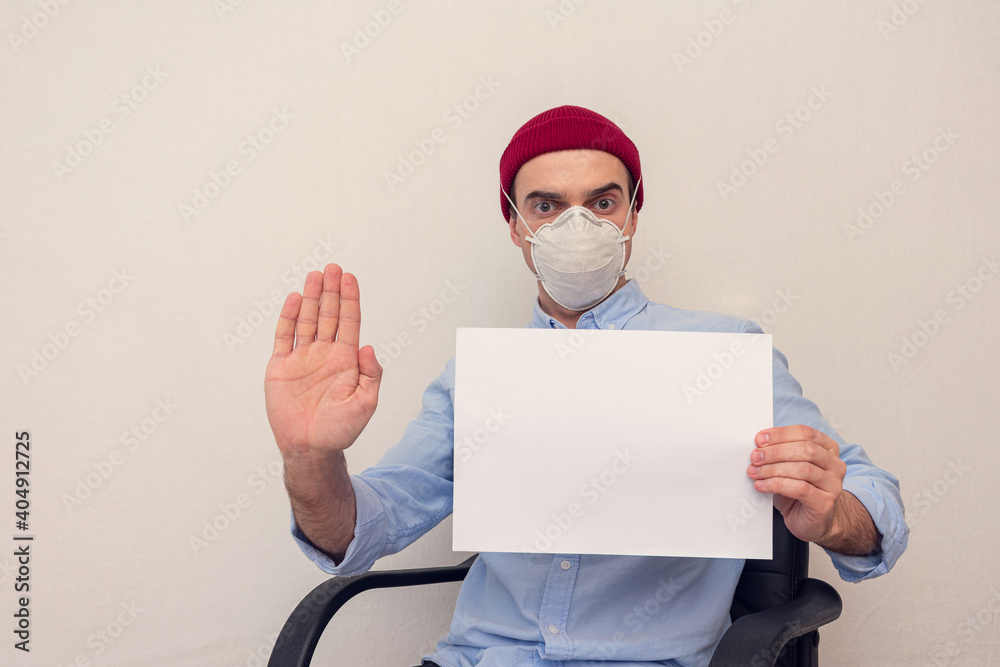 Φωτογραφία Man in a respirator shows a sheet of white paper and sign stop, white backgrou