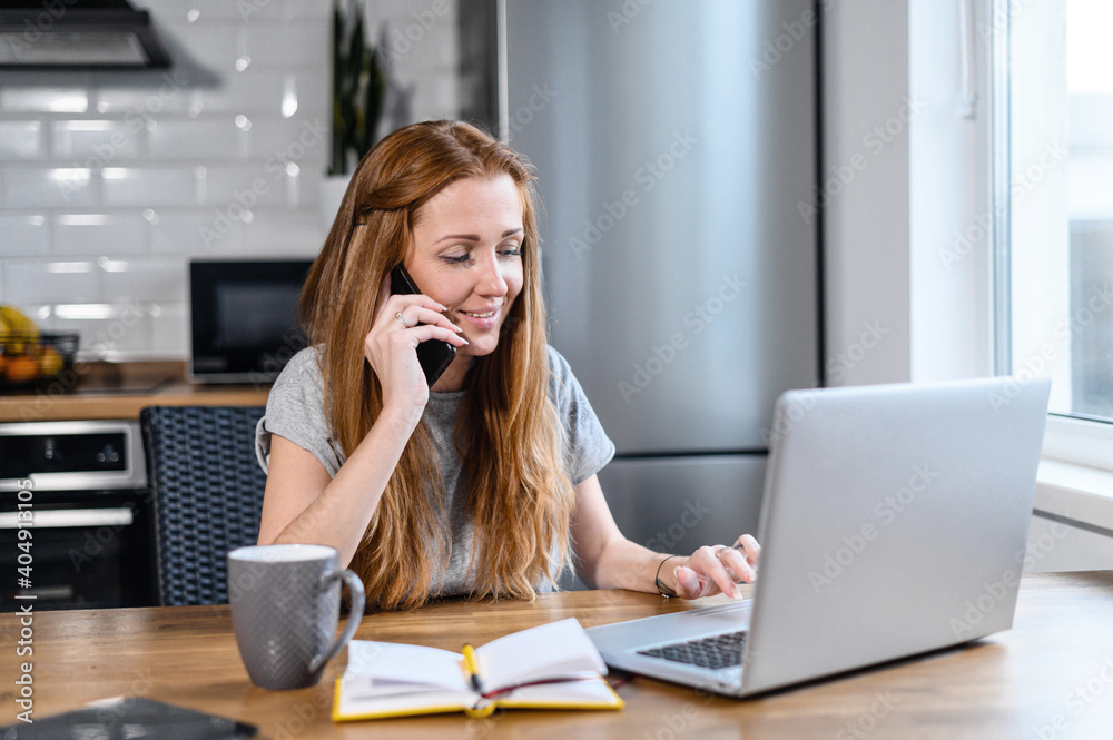 Happy confident woman sitting at work desk in home office, using smartphone and laptop, smiling. Beautiful female employee discuss a business plan with colleague, team project concept Happy confident woman sitting at work desk in home office, using smartphone and laptop, smiling. Beautiful female employee discuss a business plan with colleague, team project concept