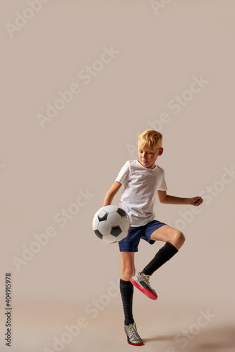 Fototapeta Naklejka Na Ścianę i Meble -  kid professionally training with ball in studio, preparing for competition, game, wearing special uniform. isolated on brown background