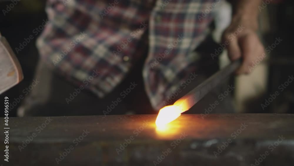 Close up of male blacksmith hammering red hot piece of metalwork on anvil - shot in slow motion Close up of male blacksmith hammering red hot piece of metalwork on anvil - shot in slow motion
