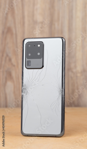Smartphone with a broken back cover on a wooden background.