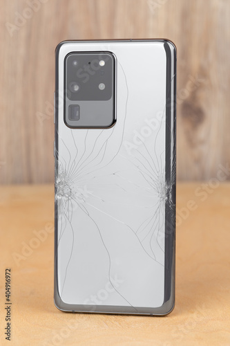 Smartphone with a broken back cover on a wooden background.