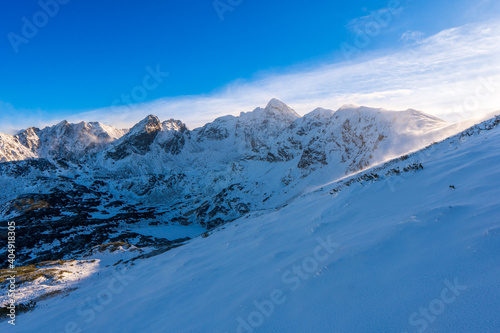 Winter mountain landscape. Sun shines through mountain peak at snowy hills. Winter scene in Tatra mountains  Poland.