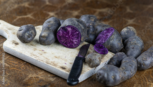 Obraz na płótnie Vitelotte, french purple potatoes sliced in half with a knife on wooden board at rustic kitchen table. Blue variety of popular potato w salonie