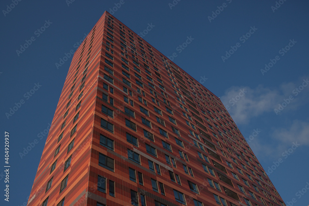 High-rise building on a background of blue sky. Tall new building with mirrored windows, bottom view. Background texture: modern office building. 