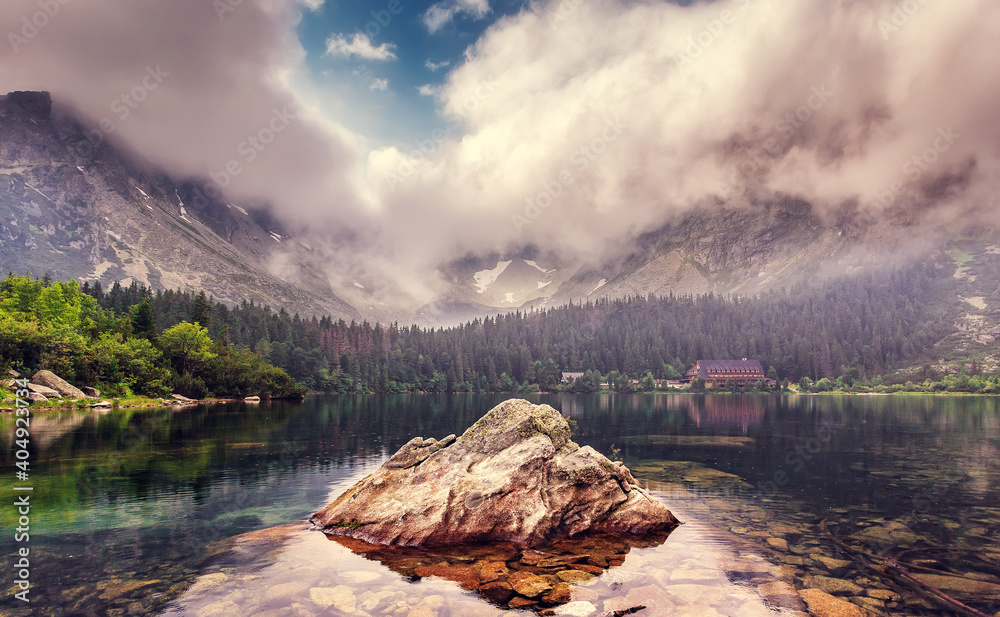 Magic atmothferic landscape. Amazing Nature background. Alpine lake with colorful overcast sky and mountains. Incredible view of beautiful mountains in High Tatras. Lake Popradske pleso, Slovakia