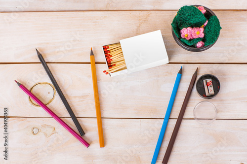 Mock up of matches box with white sides on beige wooden background, with colored pencils and knitted decorative flowers.