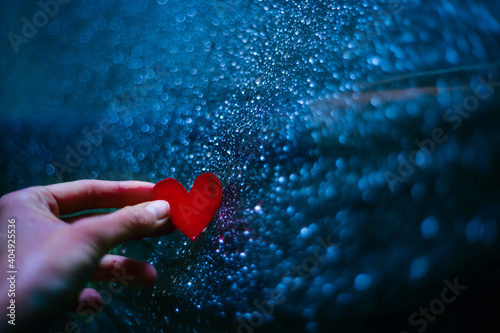 Hand holding a red paper heart on a rainy day