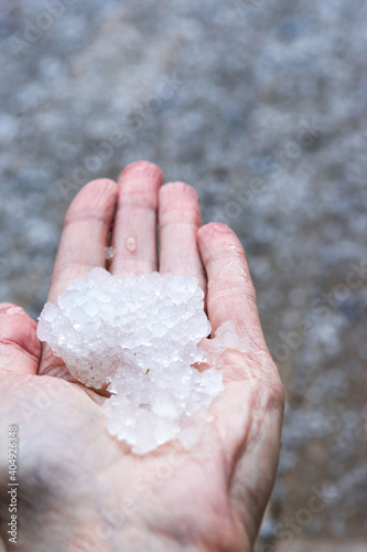 Woman is holding pieces  ice crystals of hail in springtime after hail storm, defocused ice background, vertical view
