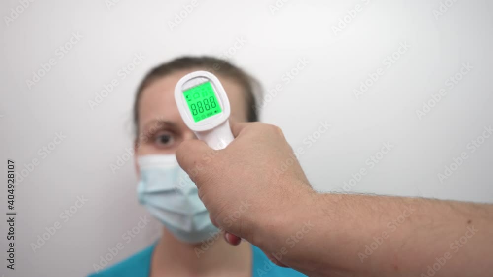 Temperature measurement with an electronic infrared thermometer in a woman. Man's hand with thermometer Temperature measurement with an electronic infrared thermometer in a woman. Man's hand with thermometer