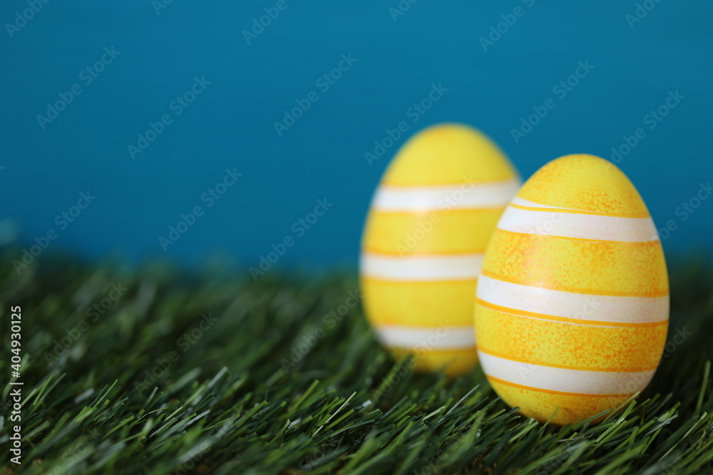 Easter holiday. Easter yellow striped eggs in green grass on a bright blue turquoise background.Spring festive easter background. copy space.Easter holiday card blank. Easter holiday. Easter yellow striped eggs in green grass on a bright blue turquoise background.Spring festive easter background. copy space.Easter holiday card blank.