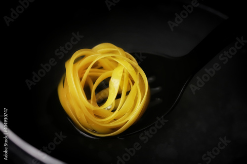 Fettuccine pasta is cooked in a saucepan. Fettuccine pasta on a slotted spoon.