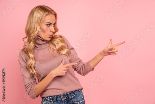 Portrait of an excited young casual girl pointing at copy space isolated over pink background