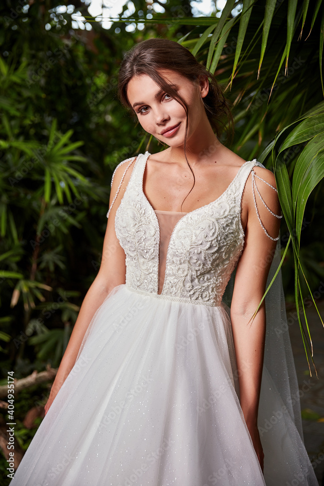 Beautiful sexy woman model bride wearing white long silk and lace wedding dress fashion espousal bright makeup brunette hairstyle ceremony in green summer garden love.