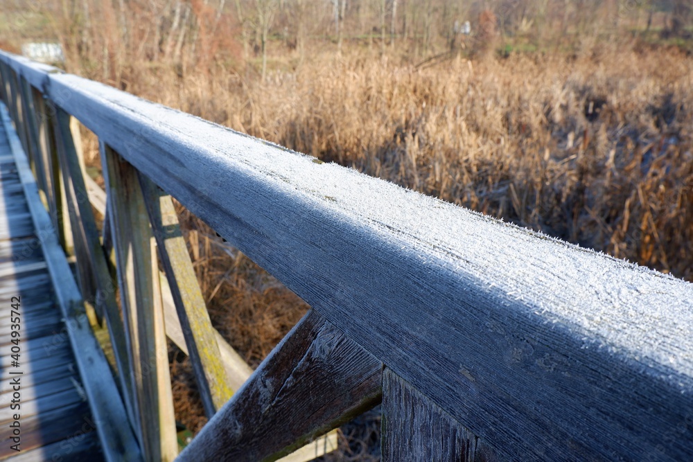 Icy hoarfrost on the railing of a wooden bridge at a stream with reeds in a frosty winter morning in Budapest suburb, Hungary Icy hoarfrost on the railing of a wooden bridge at a stream with reeds in a frosty winter morning in Budapest suburb, Hungary